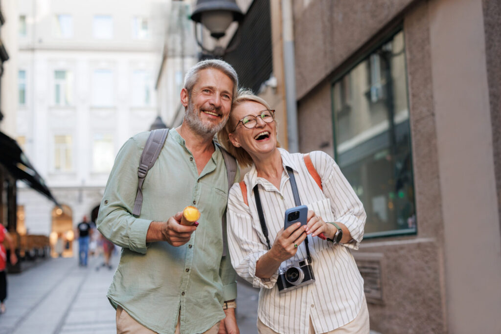 Happy mature couple enjoying a vacation, walking down a scenic city street. They are capturing memories with a camera and sharing moments.